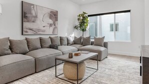 A modern living room with a sectional sofa, a coffee table, a large abstract painting, and a window with a view. - Summer Getaway: Hot tub & Cold Plunge, Gear-dryer (Salt Lake City)