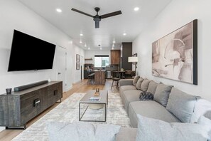 A modern living room with a flat-screen TV, a sofa, a coffee table, and a dining area in the background. - Summer Getaway: Hot tub & Cold Plunge, Gear-dryer (Salt Lake City)