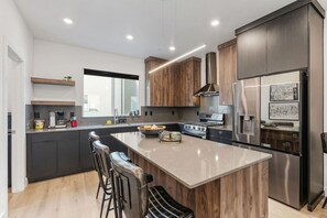 A modern kitchen with a central island, dark cabinetry, stainless steel appliances, and a large window.