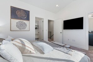 Un dormitorio con una cama, un televisor montado en la pared y obras de arte sobre la cama.