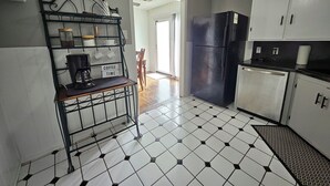Cuina amb espai per al cafè, nevera i zona de menjador amb una cadira.