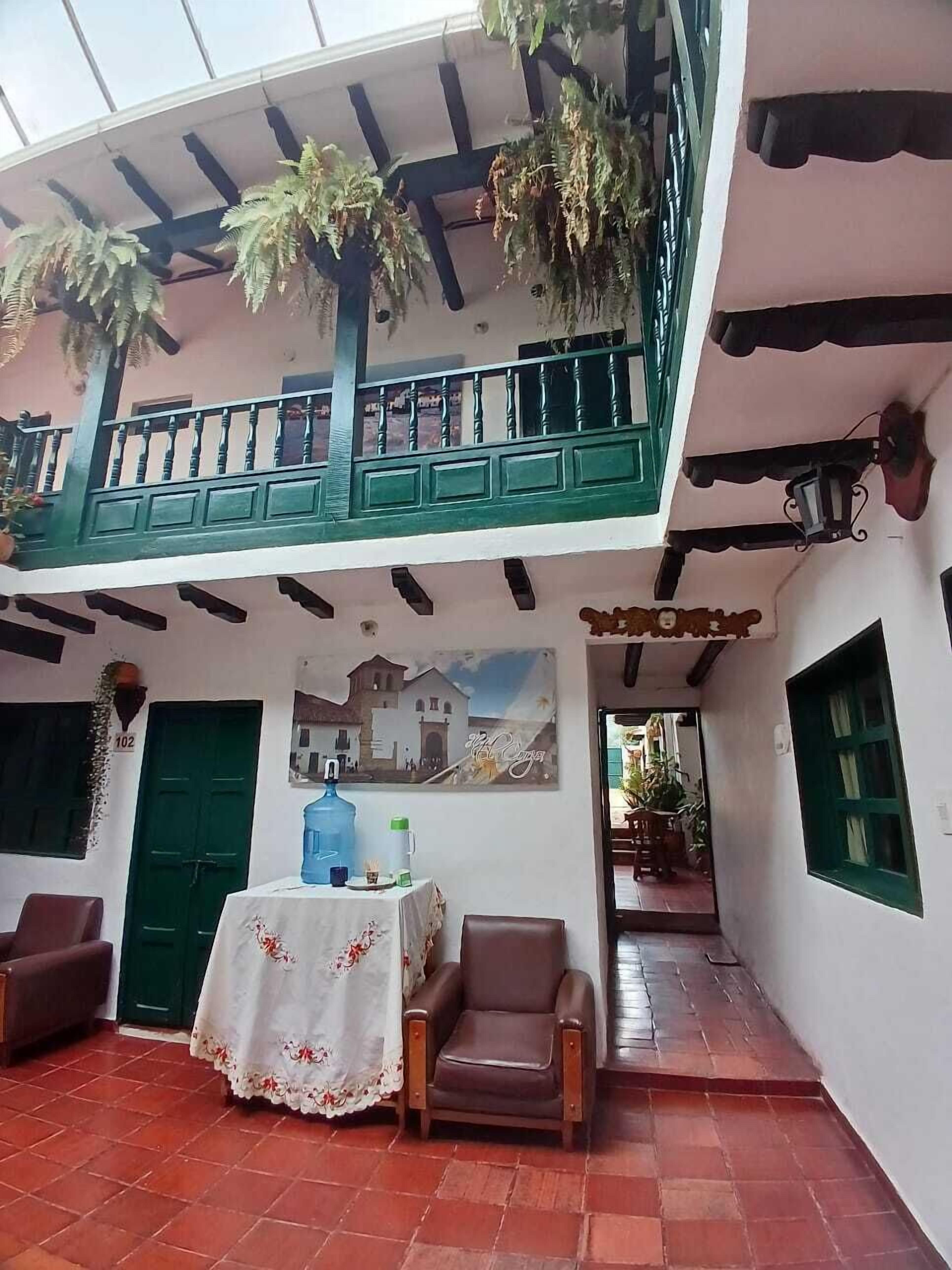 A two-story building with a balcony, a table with a floral tablecloth, and a chair.