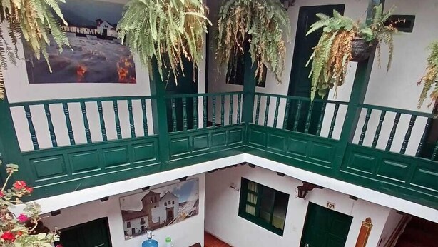 A multi-level atrium with a central courtyard, green railings, and hanging plants. - Hotel el Corzo de la Villa (Villa de Leyva)