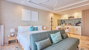 A modern hotel room with a bed, a sofa, a nightstand, a lamp, a telephone, and a kitchen area. - Surf & Fun Beachfront Stay in Mirleft With Balcony (Mirleft)