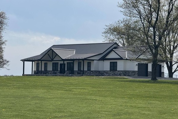 This close-up view highlights the beautiful architectural design and bold contrast of the black metal roof and stone accents. The wide porch and symmetrical layout give the home a clean and inviting presence.
