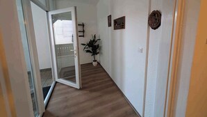 Un corridoio con pavimento in legno, una pianta in vaso e una porta che dà su un balcone.