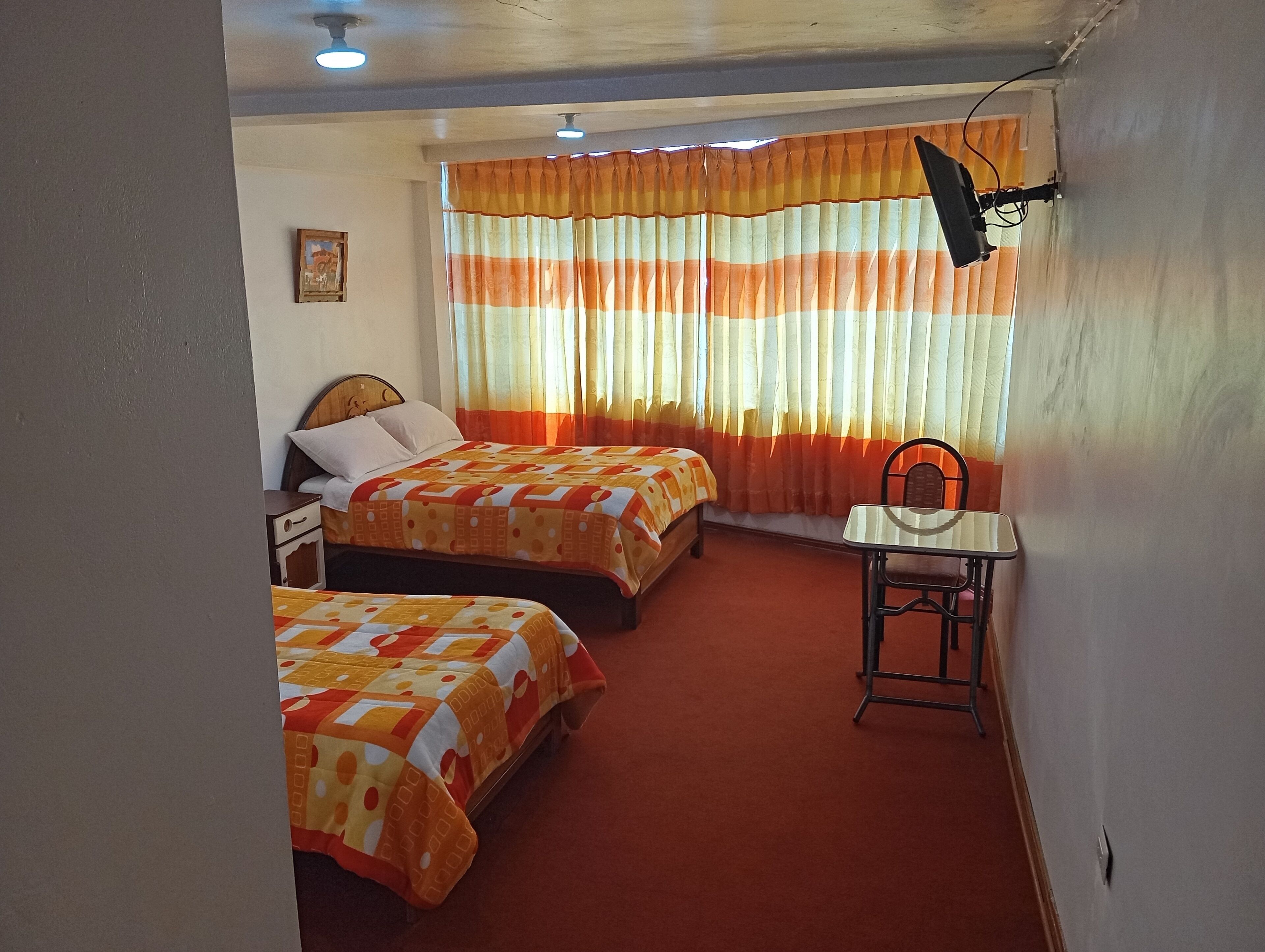 A hotel room with two beds, a small table, and a chair.