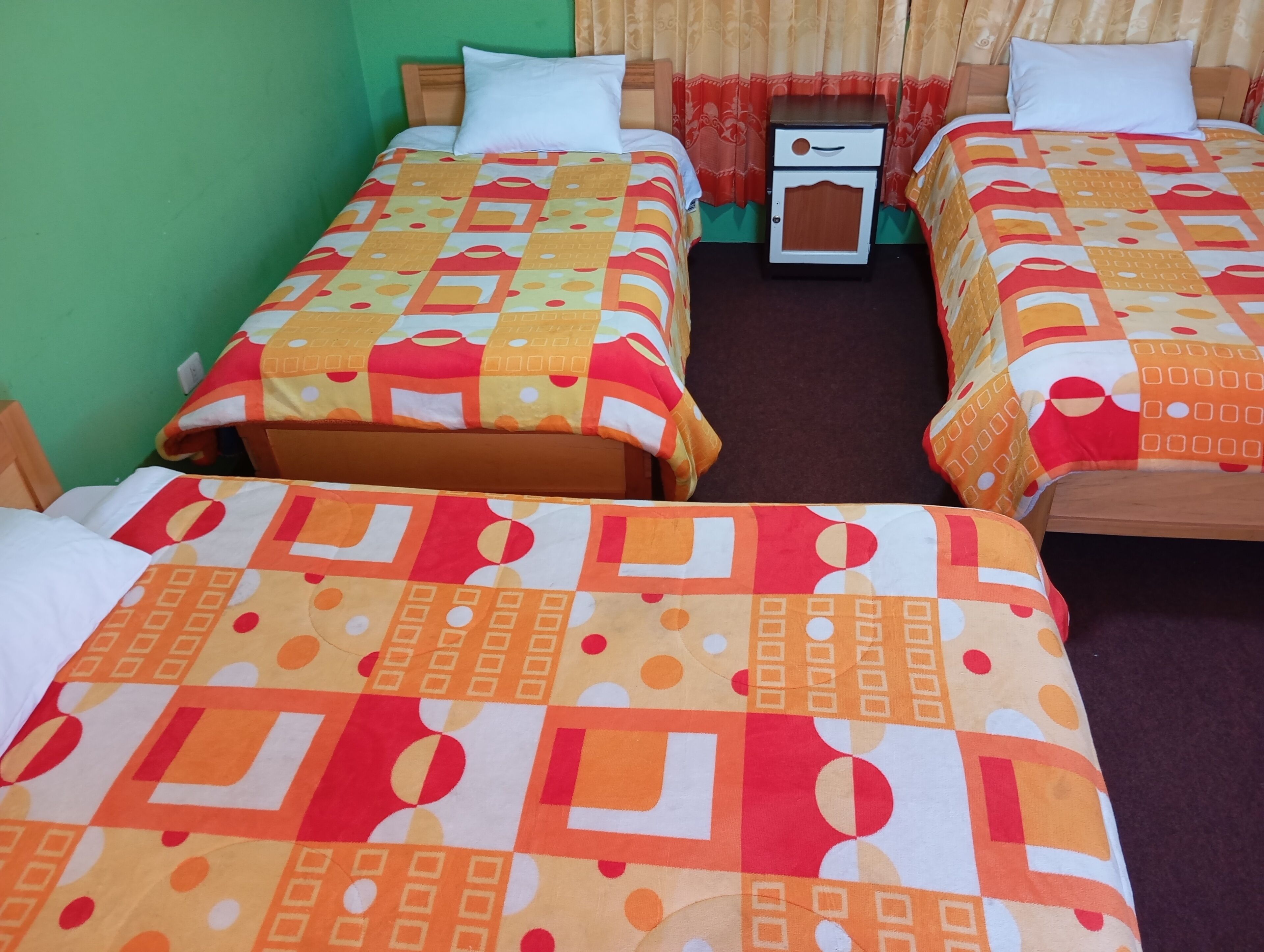 Habitación de hotel con dos camas individuales, cada una con una colcha estampada, una mesita de noche y un cabecero de madera.
