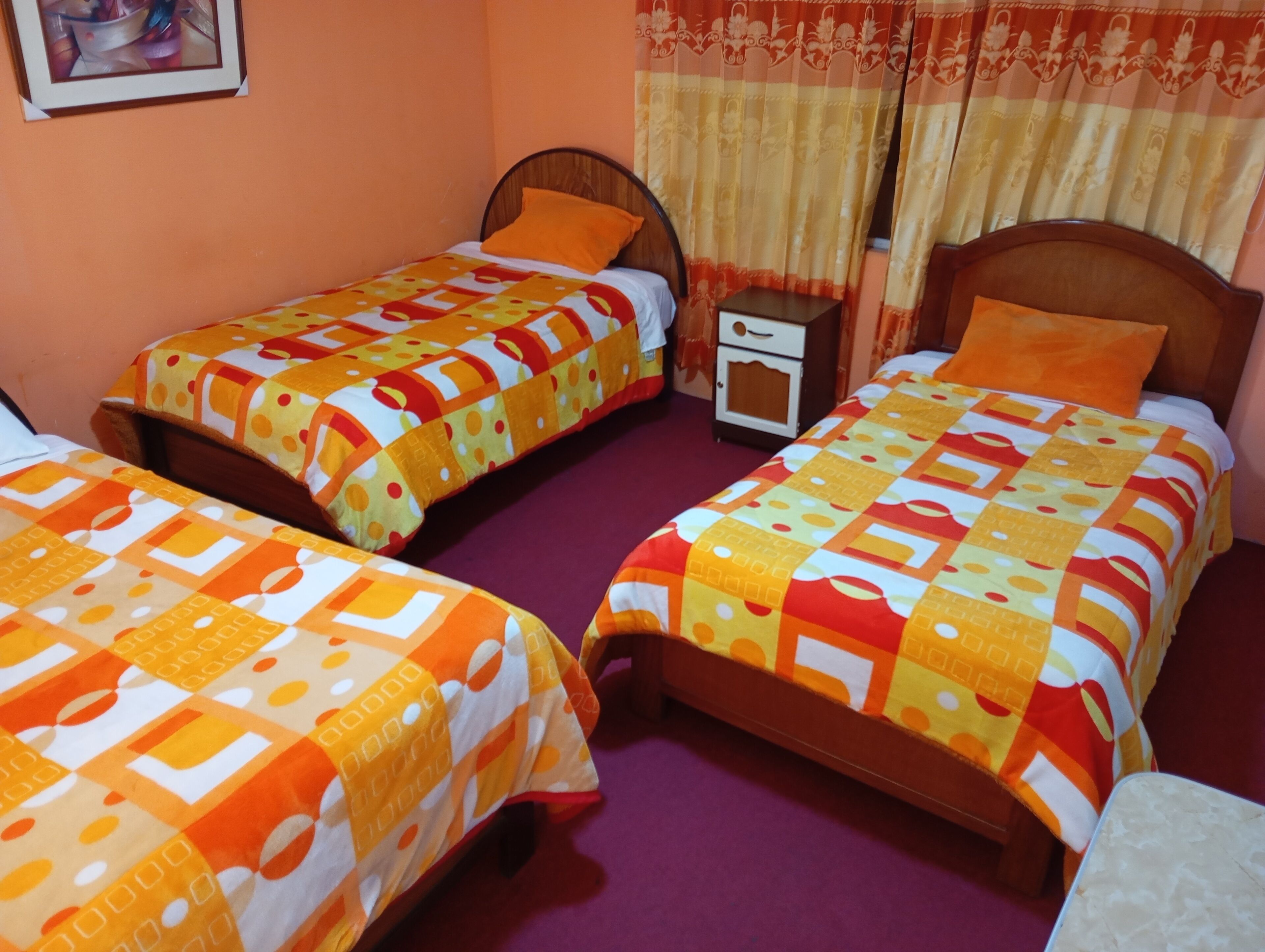 A room with two single beds, each with a wooden headboard and a colorful quilt. There is a small bedside table with a lamp between the beds.