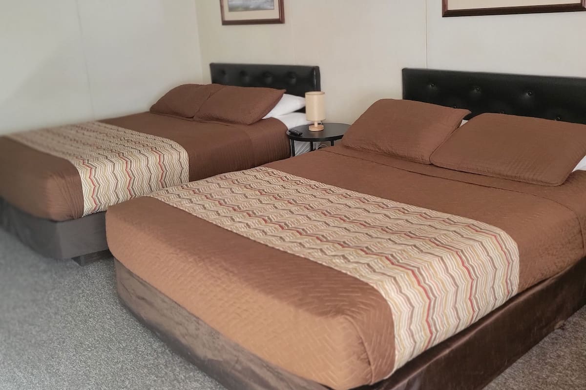 A hotel room with two beds, a nightstand, a lamp, and two framed pictures on the wall.