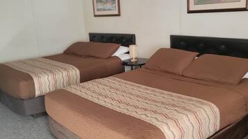 A hotel room with two beds, a nightstand, a lamp, and two framed pictures on the wall.