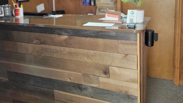 A reception desk with a wooden panel design, a sign that reads "stay awhile", and a door with a sign above it. - Amaris Inn (Redfield)