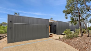 A modern building with a large metal gate, a pathway leading to the entrance, and a small garden area with a tree and shrubs. - Belmare - A Perfect Escape Surrounded by Nature (Fairhaven)