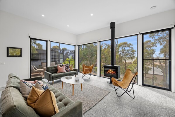 A modern living room with a fireplace, large windows, and a view of the outdoors.