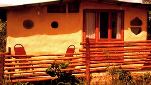 A rustic cabin with a wooden fence, two red chairs, and a window with a curtain. - Buena Vista Bio Chalet (High Paradise of Goiás)