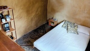 A small, cozy room with a bed, a shelf with kitchen items, and a small table. - Buena Vista Bio Chalet (High Paradise of Goiás)