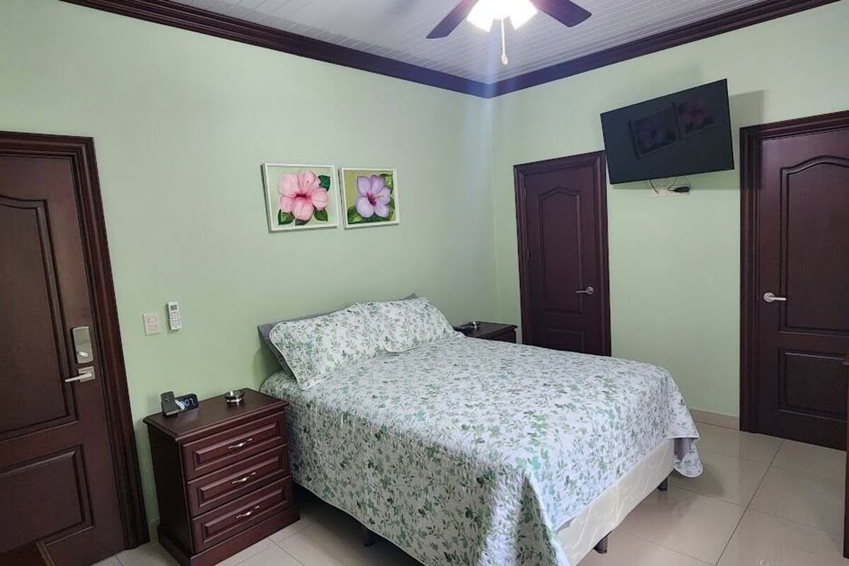 A bedroom with a bed, a nightstand, a dresser, two doors, and a TV on the wall.