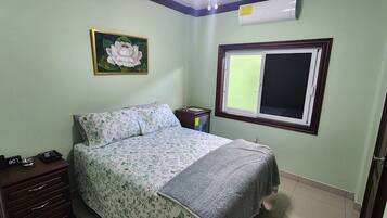 A bedroom with a bed, a nightstand, a wall clock, a window, and a painting.