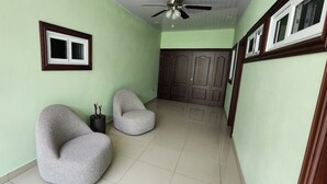 A hallway with two grey armchairs, a ceiling fan, and a door with a decorative panel. - Del Pilar Bed & Breakfast (Managua)