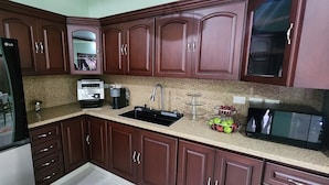 A kitchen with dark wooden cabinets, a black refrigerator, a microwave, a toaster, and a sink. - Del Pilar Bed & Breakfast (Managua)