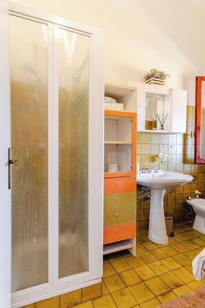 Casa de banho com soalho em azulejos amarelos, lavatório branco, sanita e armário com espelho.