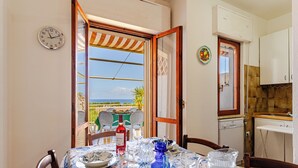 A dining area with a table set for two, a clock on the wall, and a view of the sea through an open door. - Villa see view - 5min walk to the beach (Scaro-reggio-Scornavacca-vardano)