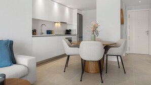 A modern kitchen with white cabinets, a built-in oven, and a coffee machine. There is a dining area with a wooden table and four chairs. - Top Floor Seaview Apartment (Estepona)