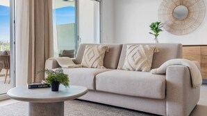 Una sala moderna con un sofá color beige, una mesa de centro redonda y una planta en maceta.