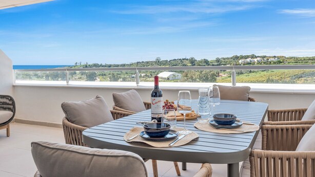 Un comedor con una mesa dispuesta para dos, una botella de vino y una vista panorámica de la costa.