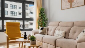 Una sala de estar moderna con un sofá beige, un sillón amarillo, una mesita redonda y una planta en maceta.