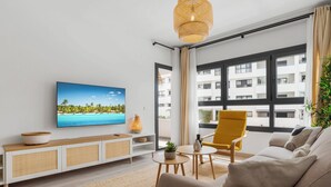 Una sala de estar moderna con un ventanal grande, un sofá, un sillón amarillo, un televisor y una lámpara de ratán.