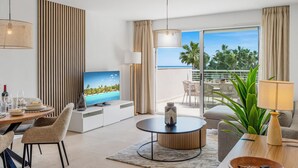 A modern living room with a TV, dining area, and balcony with a view of the ocean.