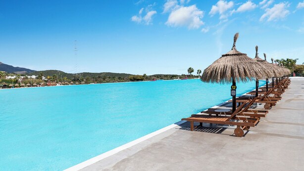 A clear blue pool with lounge chairs and thatched umbrellas, surrounded by a concrete deck.