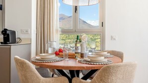 A dining area with a wooden table set for four, a coffee machine, and a view of mountains through a window.
