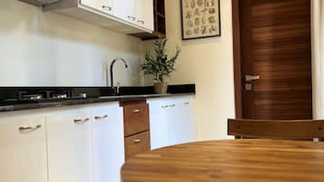 Una cocina con armarios blancos, una campana extractora de acero inoxidable, una mesa de comedor de madera y una planta en maceta.