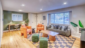 A modern living room with a wooden floor, a gray sofa, orange chairs, a coffee table, and a large window with blinds. - New Remodel! +5 bedroom+Game Room+Sauna+Theater (Denver)