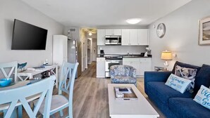 Un espace de vie compact comprenant un coin repas, une kitchenette et un canapé agrémenté de coussins décoratifs.