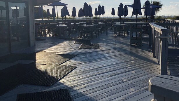 Une terrasse en bois, dotée de tables et de parasols, qui offre une vue sur la plage.
