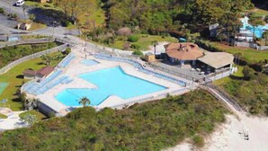 Vue aérienne d’un complexe hôtelier doté d’une grande piscine, d’une plage et d’un bâtiment dont le toit est incurvé.