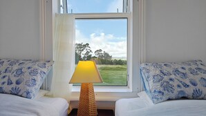 Une chambre avec deux lits, une fenêtre donnant sur un champ verdoyant et des arbres, et une lampe placée entre les lits.