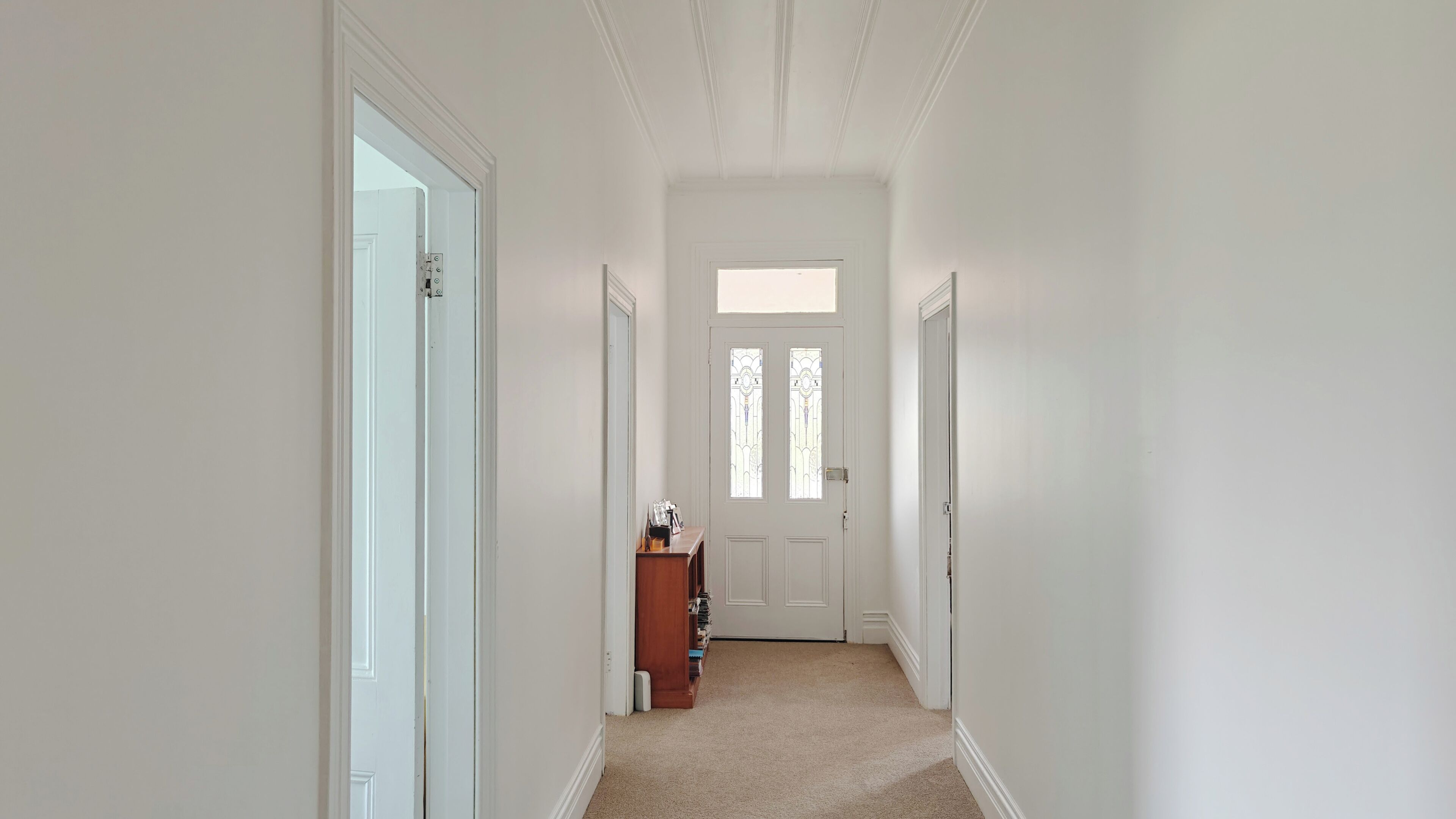 A narrow hallway with white walls and a carpeted floor, leading to a door with a stained glass window.