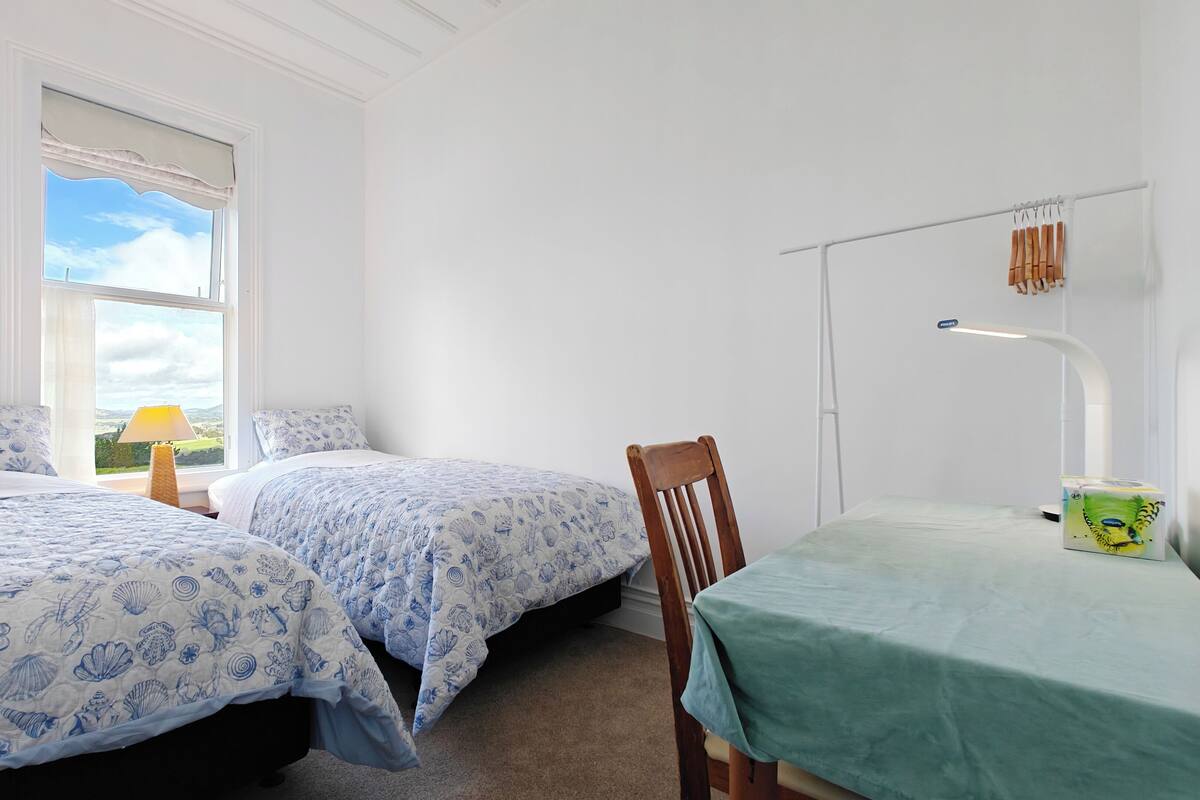 Ein Schlafzimmer mit zwei Betten, einem Tisch, einem Stuhl, einer Lampe und einem Fenster mit Blick.