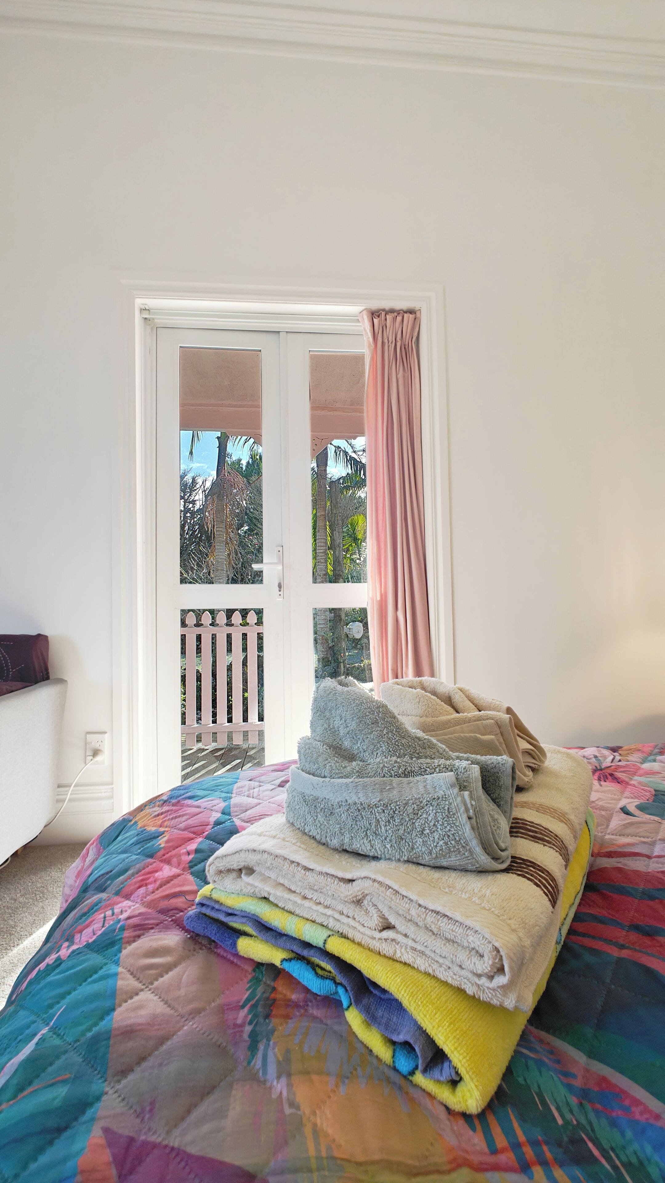 Un dormitorio con una cama, un ventanal con vistas a un balcón y un montón de toallas dobladas.
