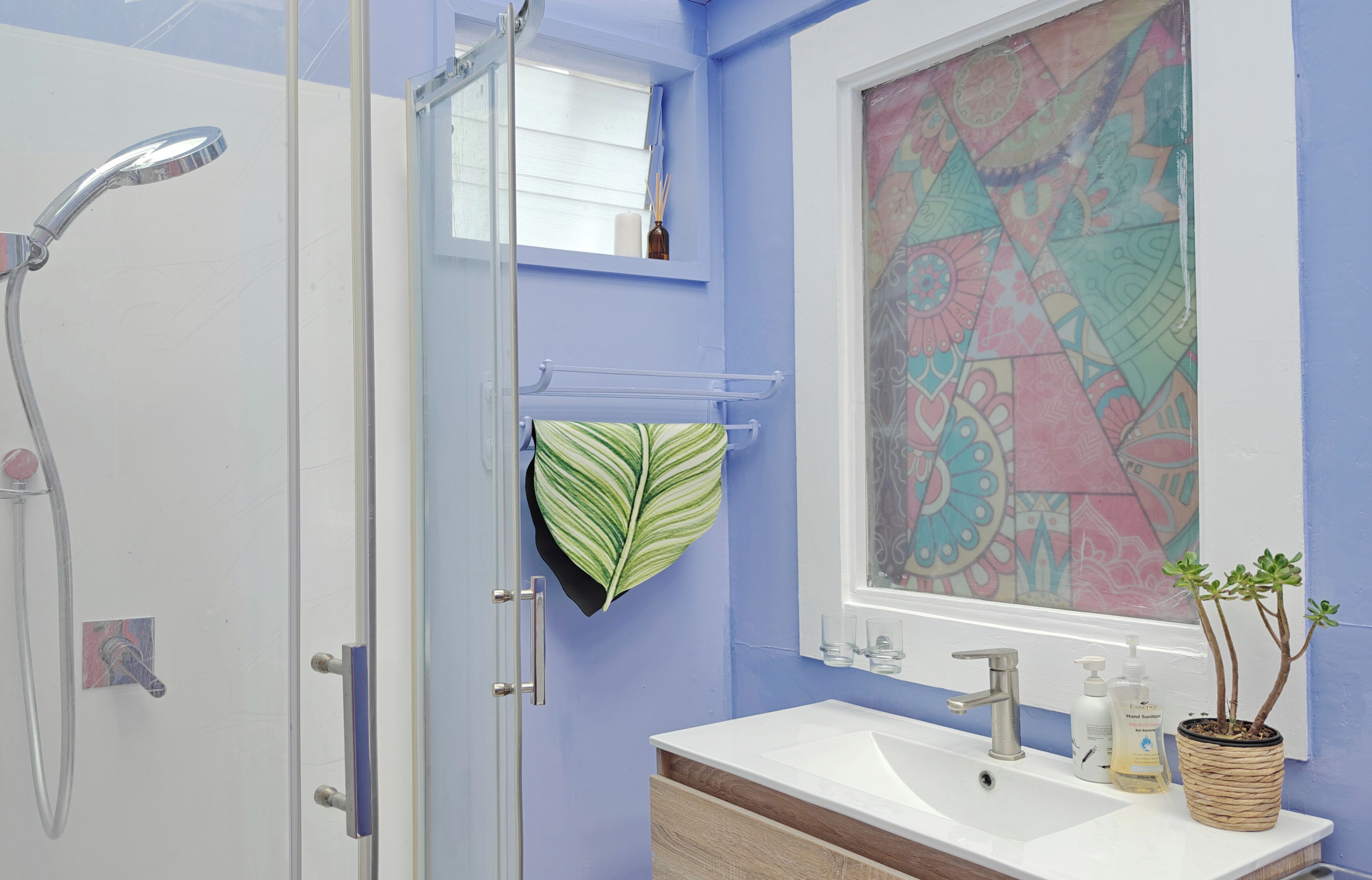 A bathroom with a shower, a sink with a mirror, and a window with a colorful geometric pattern.