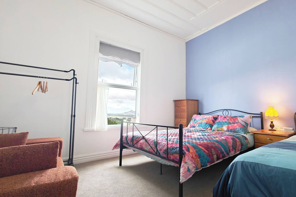 Ein Schlafzimmer mit einem Bett, einem Schminktisch, einem Fenster mit Blick und einem Sessel.