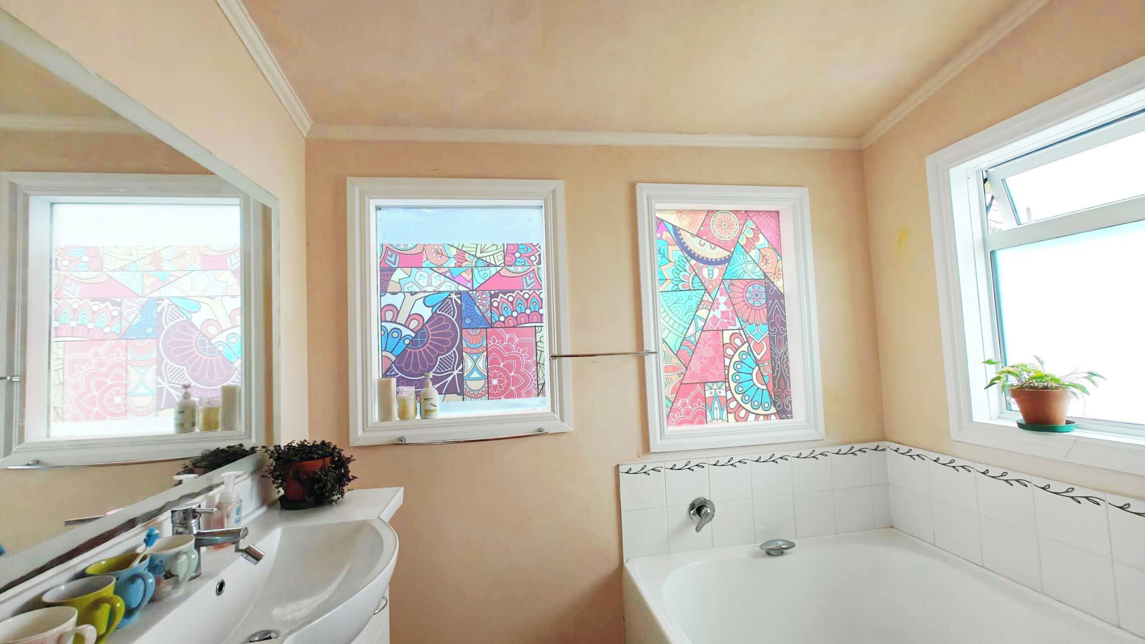 A bathroom with a white sink, a bathtub, and two windows with colorful stained glass.