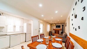 Una cocina moderna con armarios blancos, un comedor con mesa de madera dispuesta para cuatro personas y una sala de estar con sofá y televisor.