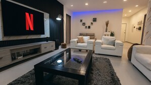 A modern living room with a large flat-screen TV displaying the Netflix logo, a black coffee table, two white sofas, and a dark rug. - Experience luxury & comfort at Maison D'Ophir's 3 bedrooms, billiard and more (Dakar)