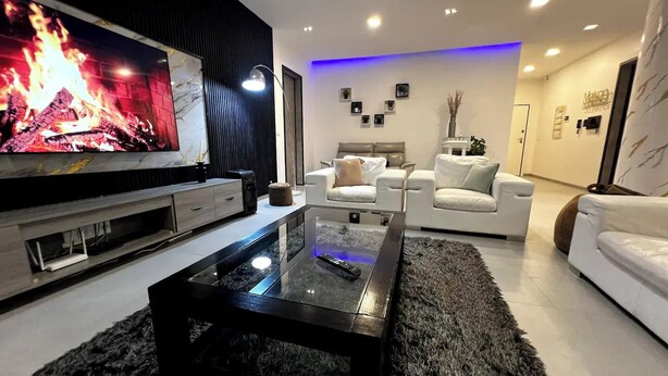 A modern living room with a flat-screen TV, a glass coffee table, and white leather sofas. - Experience luxury & comfort at Maison D'Ophir's 3 bedrooms, billiard and more (Dakar)