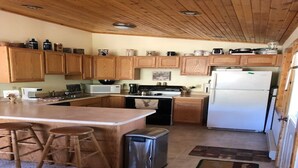 A kitchen with wooden cabinets, a central island with stools, a stove, microwave, and a refrigerator. - {Aspen Chalet} Hot Tub, Tesla Charger, Near Deadwood! (Lead)